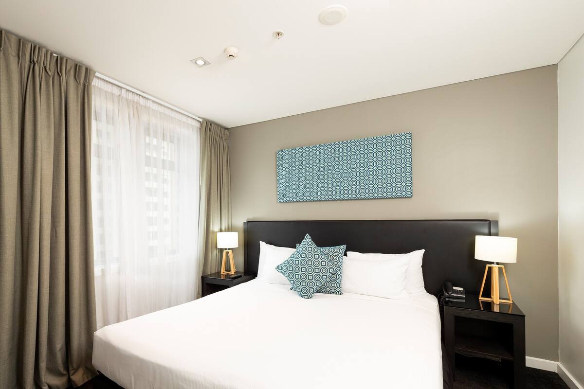 A hotel room with a large bed, two bedside tables with lamps, a wall-mounted artwork, and a window with curtains.