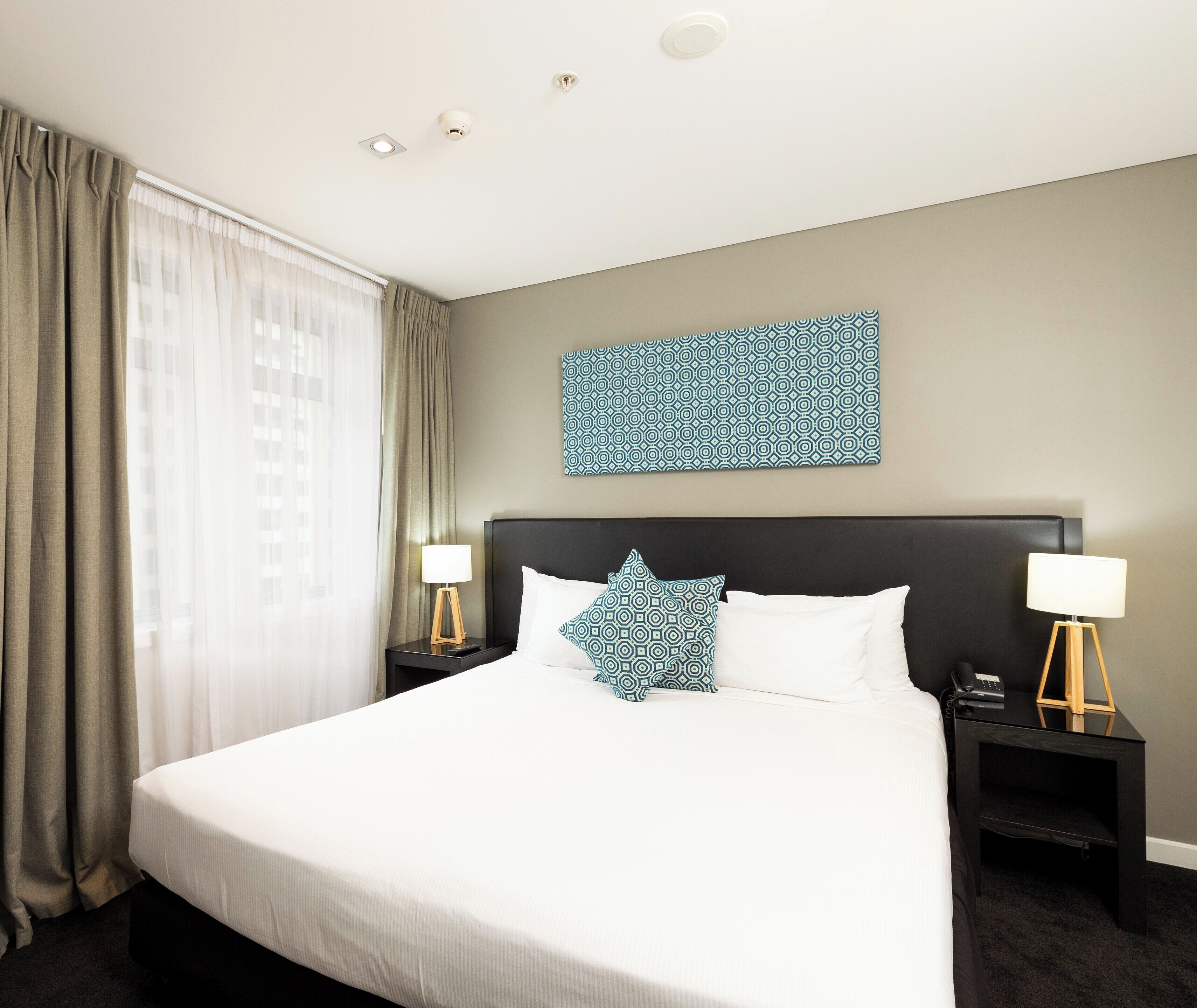 Een hotelkamer met een groot bed, twee nachtkastjes, een kunstwerk aan de muur en een raam met gordijnen.