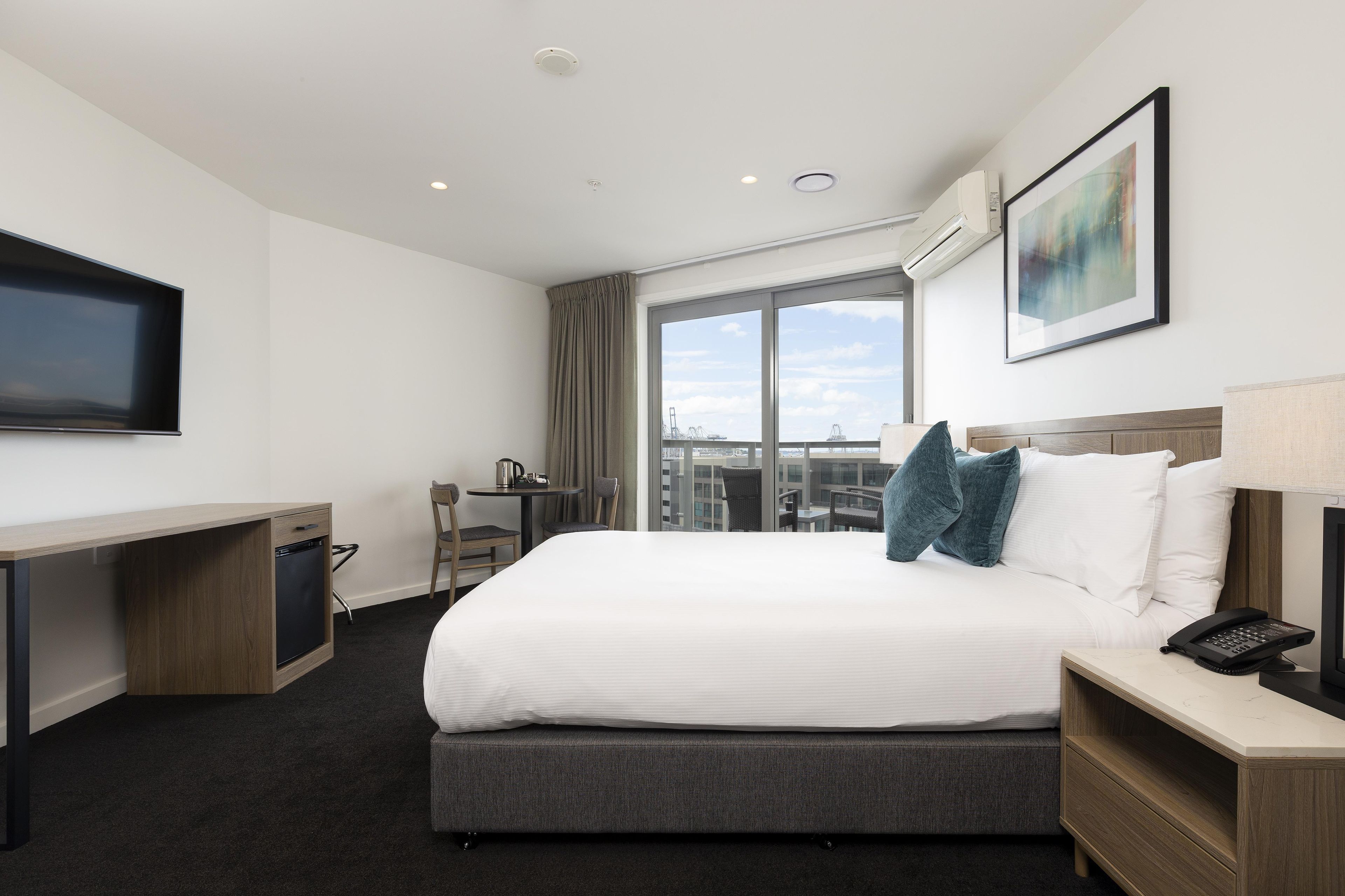 Habitación de hotel con cama, escritorio, silla, ventana con vistas y televisor de pantalla plana.