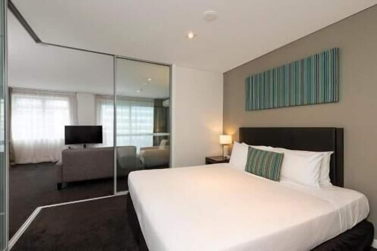 A hotel room with a large bed, a television, a desk, and a mirror.