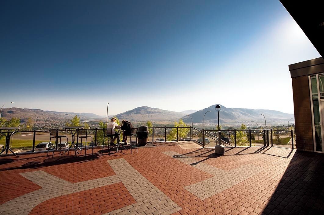 An outdoor terrace with a view of mountains, a paved floor, and a railing.