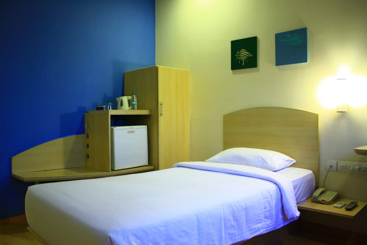 A hotel room with a bed, a small desk with a lamp, a refrigerator, and a phone on the nightstand.