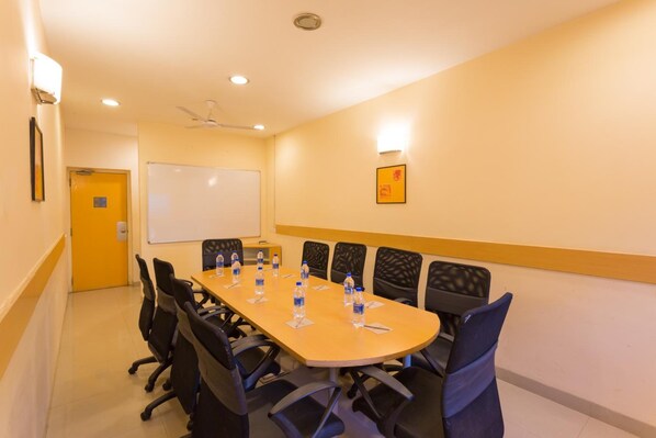 A conference room with a long table, black chairs, water bottles, a whiteboard, and a ceiling fan. - Ginger Pune Pimpri (Pune)