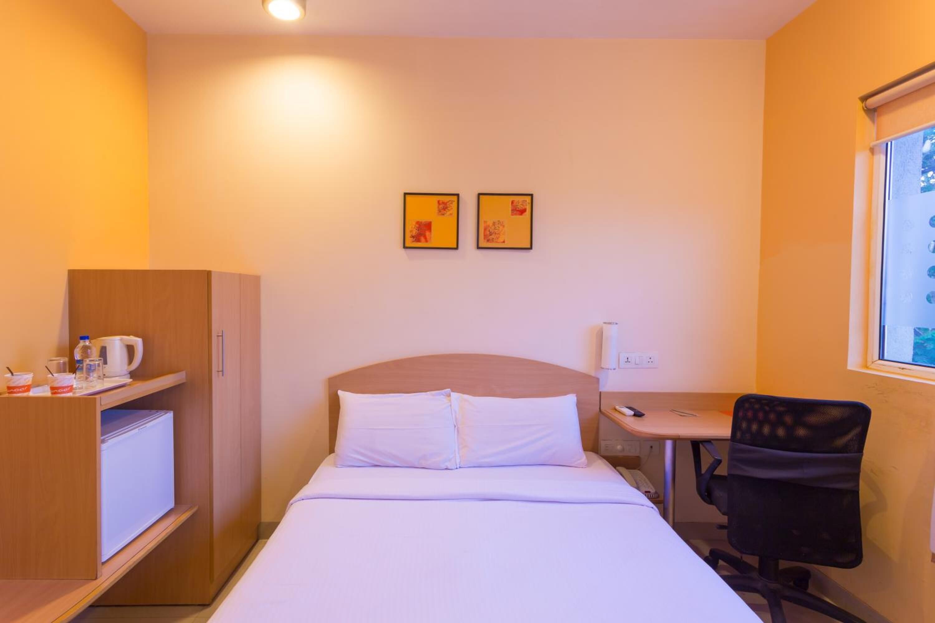 Ein Hotelzimmer mit Bett, Schreibtisch, Stuhl, Kleiderschrank und zwei gerahmten Bildern an der Wand.