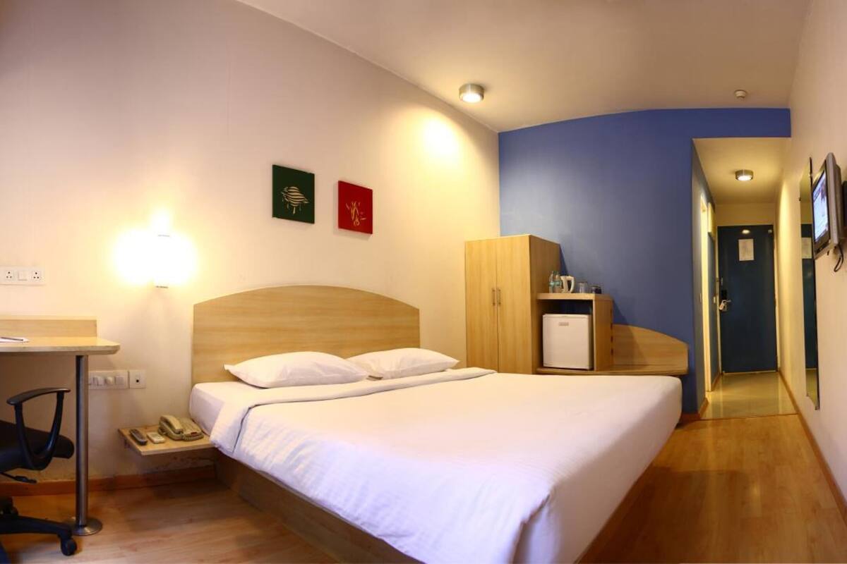 A hotel room with a bed, desk, chair, wardrobe, and a small kitchenette.