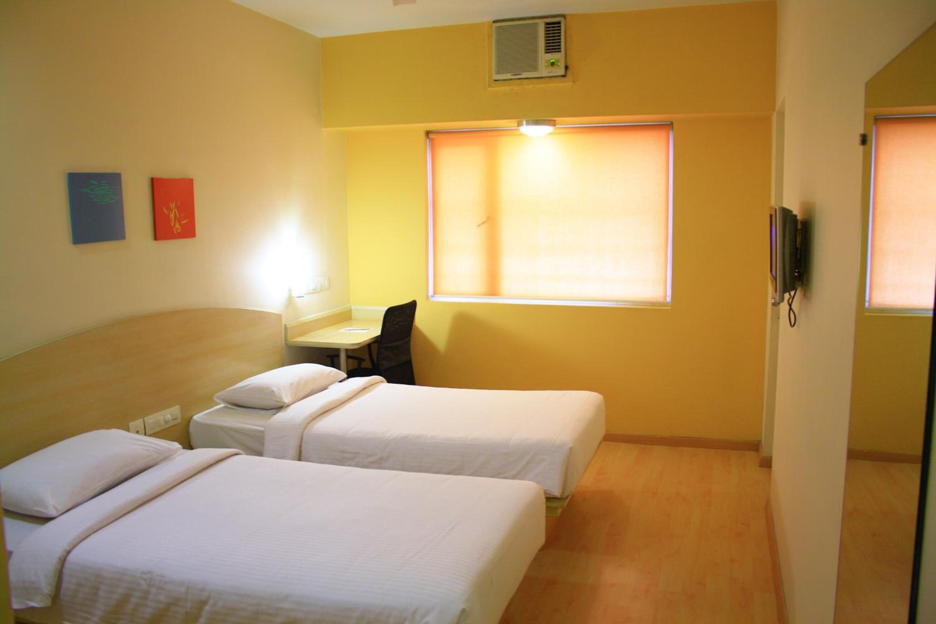 Habitación de hotel con dos camas individuales, un escritorio, una silla y una ventana con persianas.