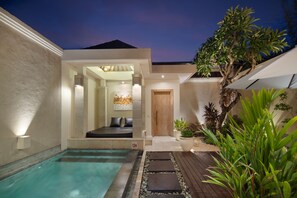 Un área de piscina moderna al aire libre con una terraza de madera, zona de estar y un jardín bien cuidado.
