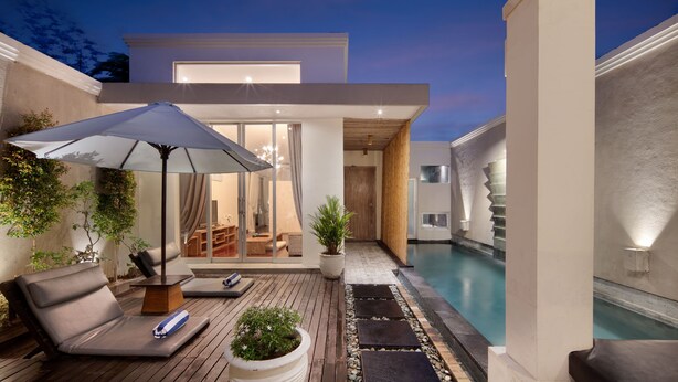 Un área de piscina moderna al aire libre con sillones reclinables, un gran paraguas y una terraza de madera.