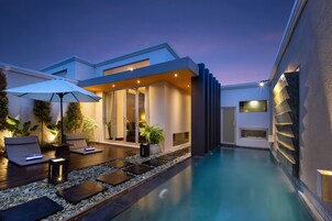 A modern outdoor pool area with lounge chairs, a table, and a potted plant.