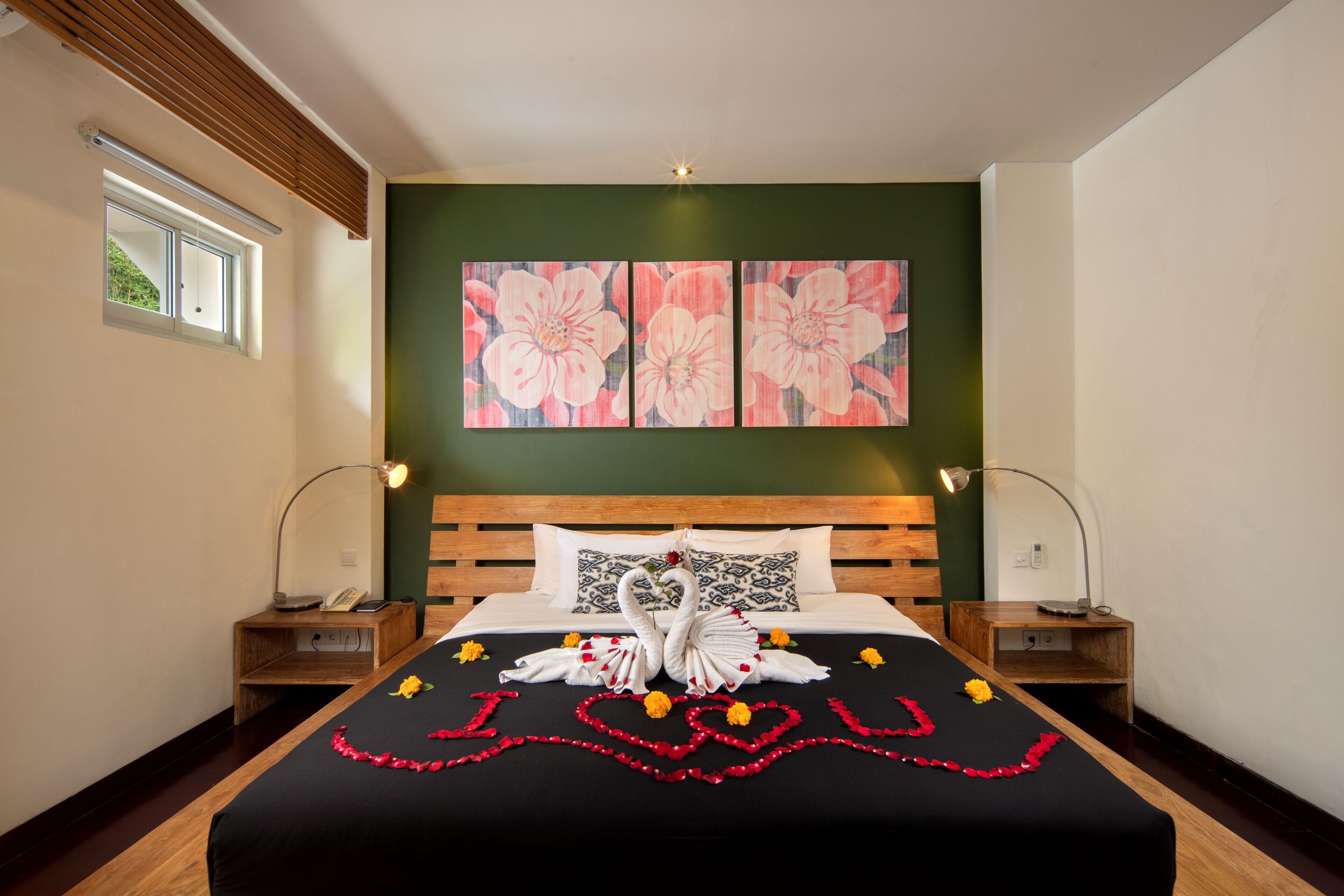 Habitación de hotel con cabecera de madera, cama con colcha negra y un cuadro floral sobre la cama. Hay dos mesitas de noche con lámparas.