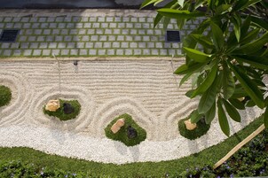 Un giardino con un vialetto di pietre, tre formazioni rocciose e un muro in mattoni sullo sfondo.