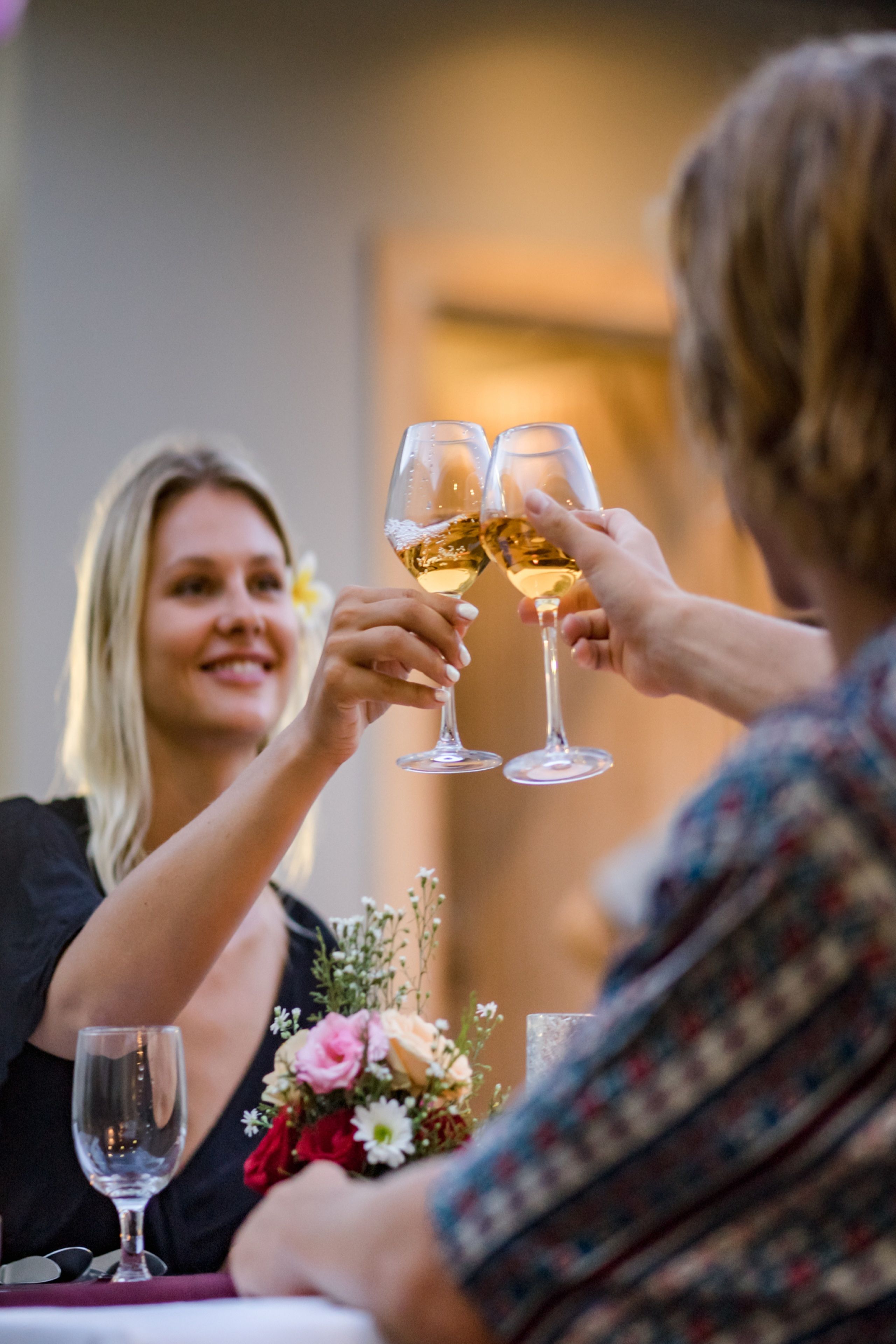 Two people toasting with wine glasses at a table with a floral centerpiece.