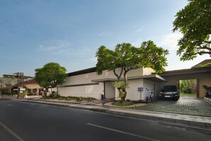 Un edificio moderno con una zona de estacionamiento techada, una bicicleta y un árbol en la parte delantera.
