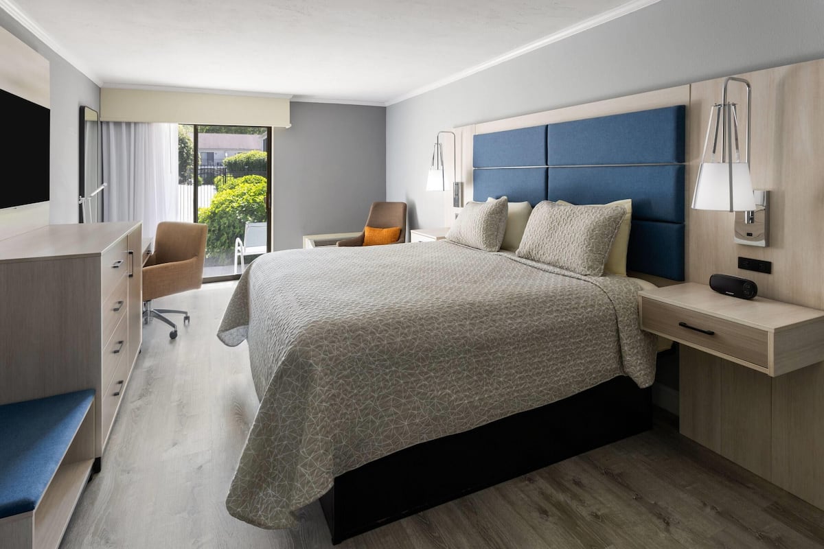 Une chambre d’hôtel moderne, dotée d’un grand lit, d’un bureau, d’une chaise et offrant une vue sur la verdure environnante.