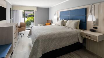 Una habitación de hotel moderna con una cama grande, un escritorio, una silla y vistas a zonas verdes.