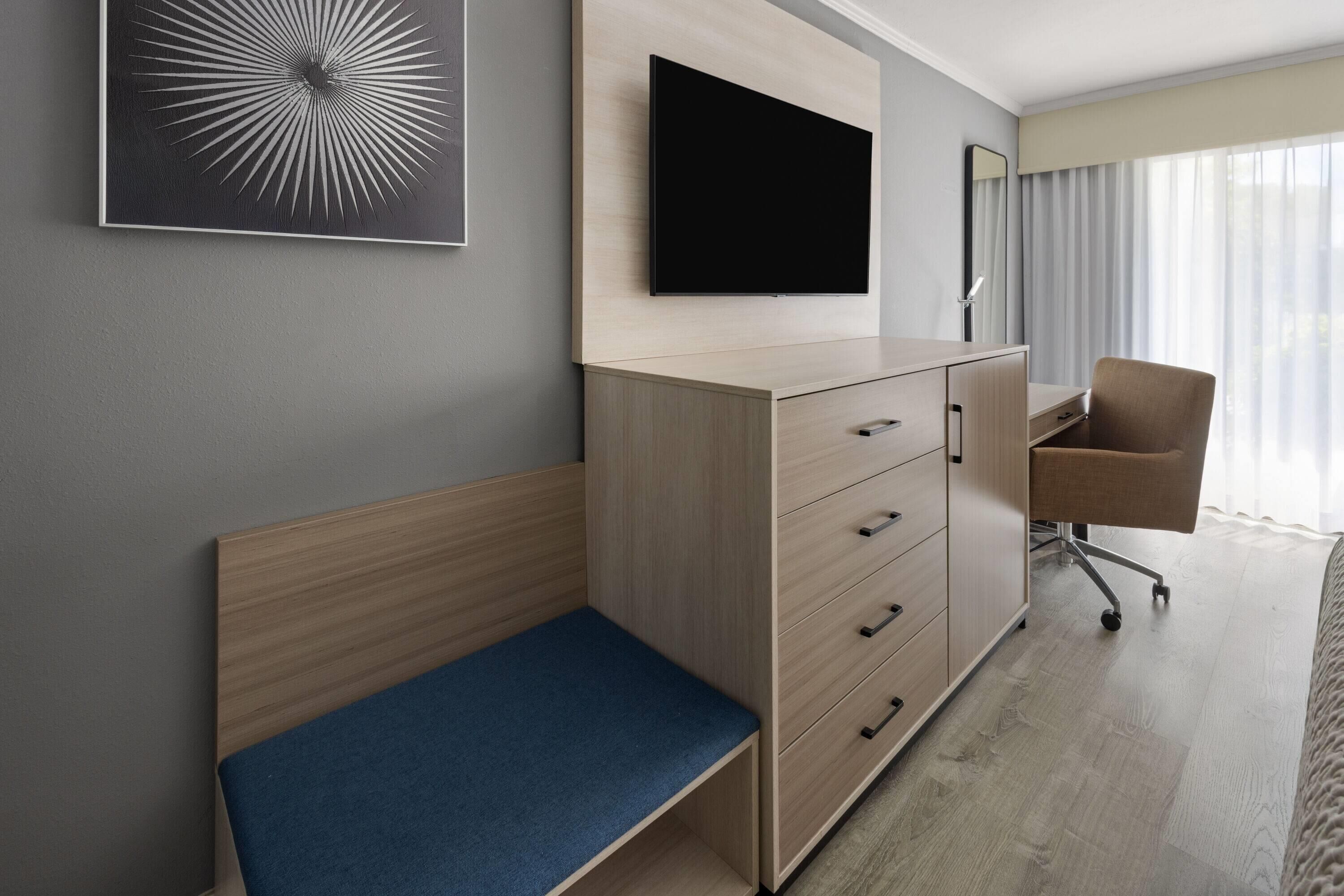 A hotel room with a bed, a desk, a chair, a TV, and a wall-mounted cabinet.