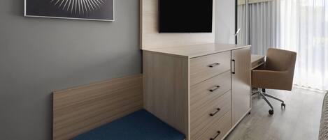Quarto de hotel com cama, escrivaninha, cadeira, televisão e armário fixado na parede.