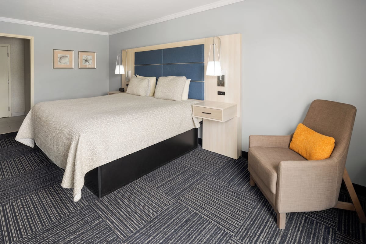 Une chambre d’hôtel avec un grand lit, une table de chevet, une chaise avec un coussin orange et deux lampes fixées au mur.
