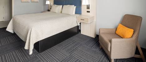 A hotel room with a large bed, a bedside table, a chair with an orange cushion, and two wall-mounted lamps.