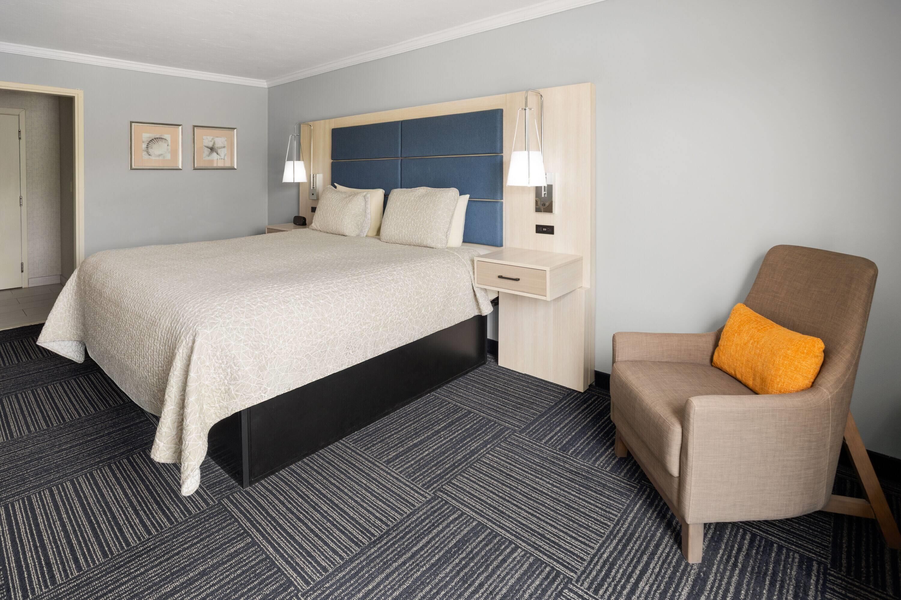 A hotel room with a large bed, a nightstand, a chair, and two wall-mounted lamps.