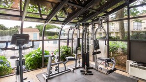 Un gimnasio con diverso equipo de ejercicio, amplias ventanas y vistas al exterior.
