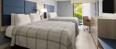 A hotel room with two beds, a desk, a chair, a TV, and a window with a view of greenery.