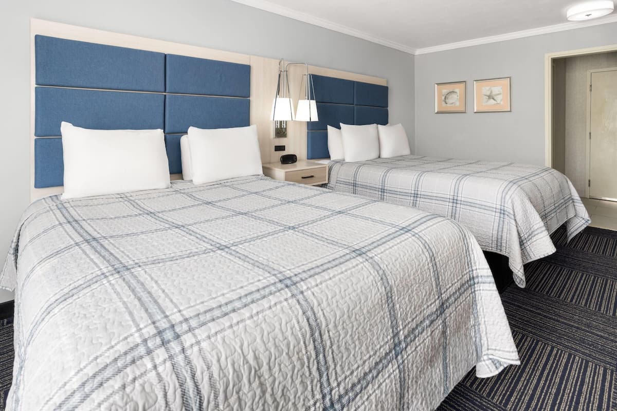 Une chambre d’hôtel avec deux lits, une table de chevet, une lampe et une porte.