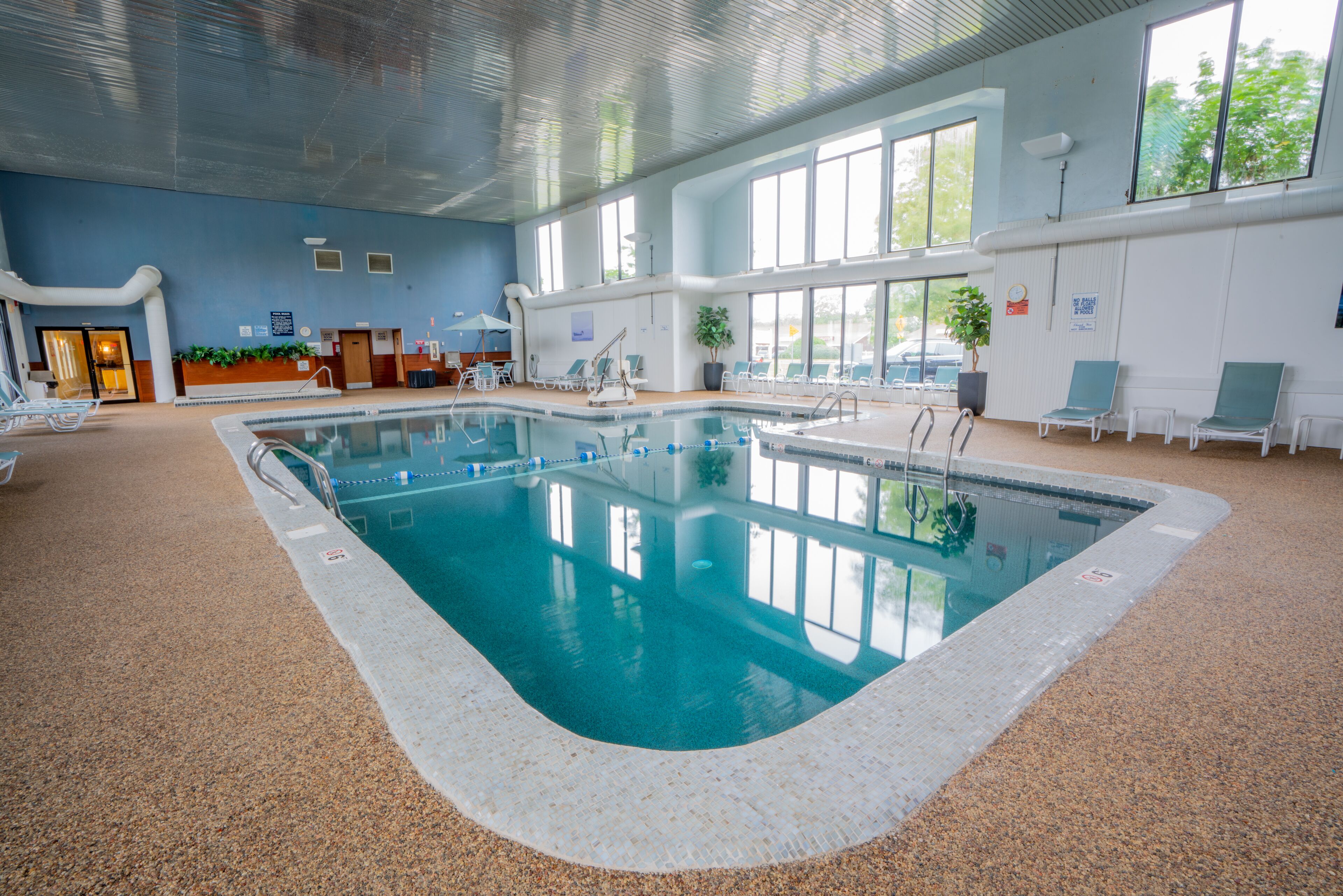 Una piscina interior con agua cristalina, rodeada de sillones de descanso y una zona de recepción.