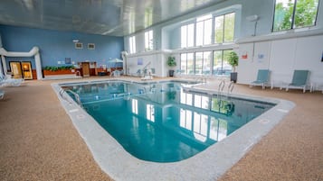 Una piscina interior con agua cristalina, rodeada de sillones de descanso y una zona de recepción.