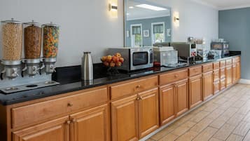Una cocina con una encimera larga, armarios de madera, un microondas y una cafetera.