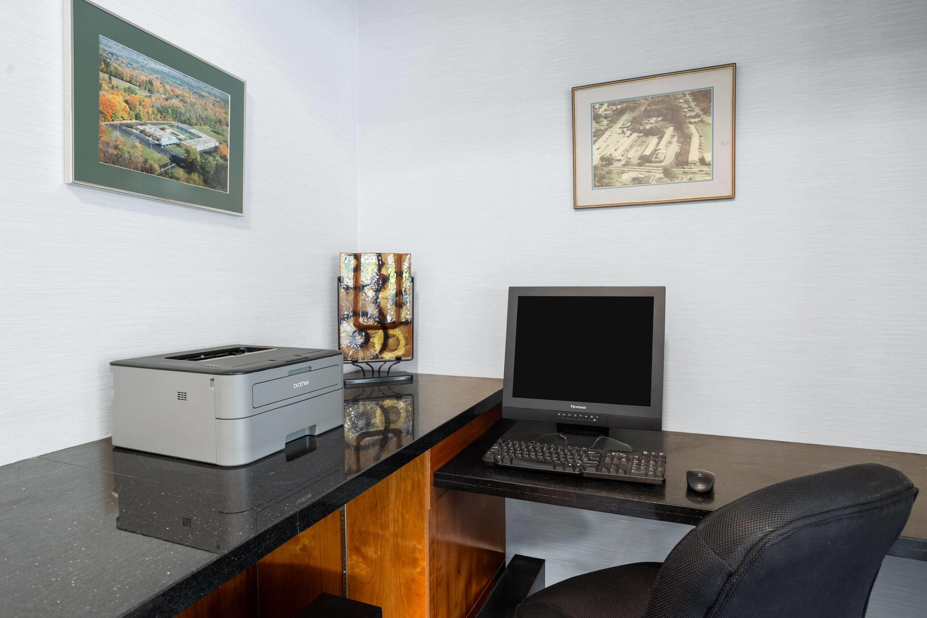 Een modern bureau met een printer, toetsenbord en monitor. Twee ingelijste foto’s hangen aan de muur.