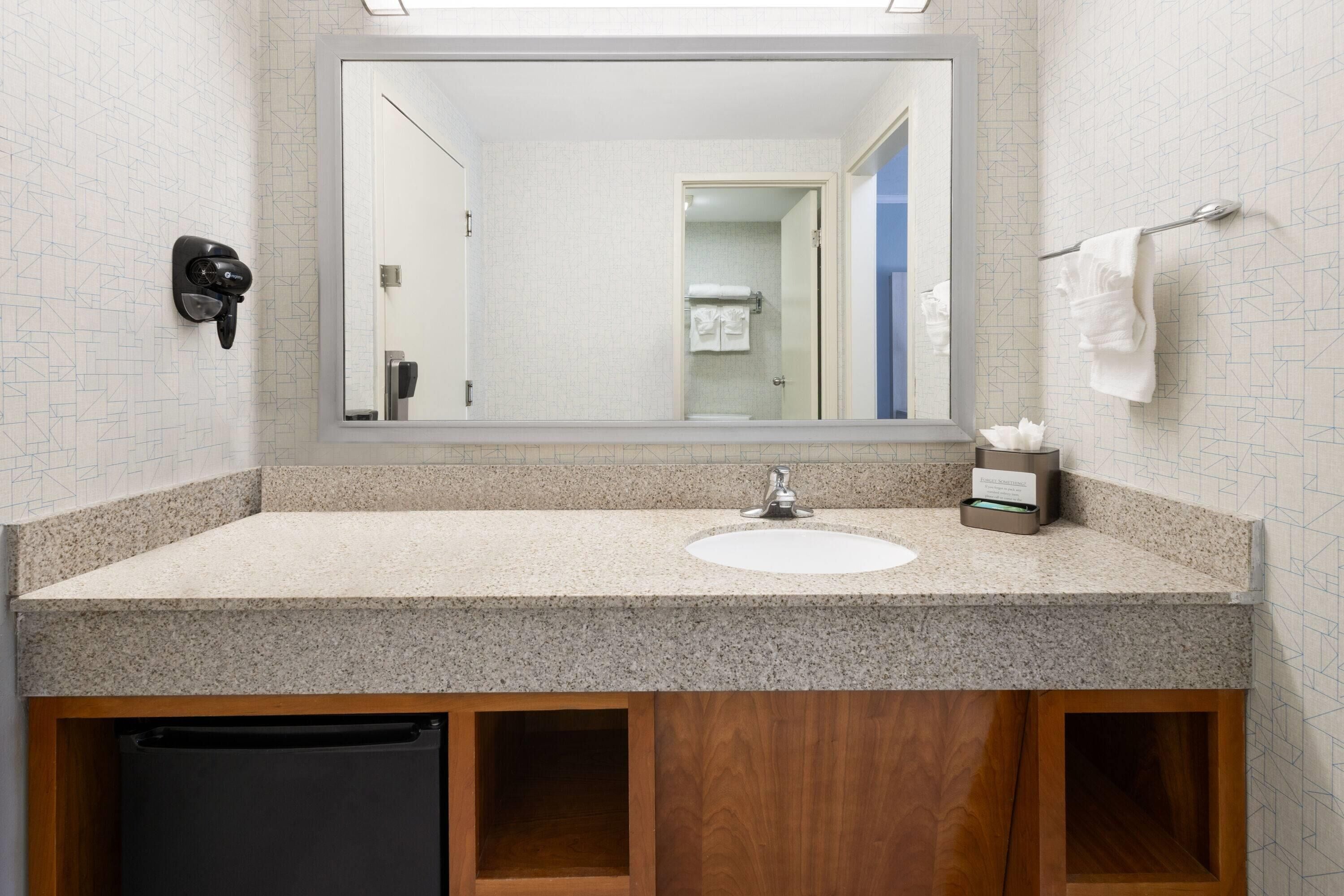 A bathroom with a granite countertop sink, a mirror above it, and a towel rack to the right.