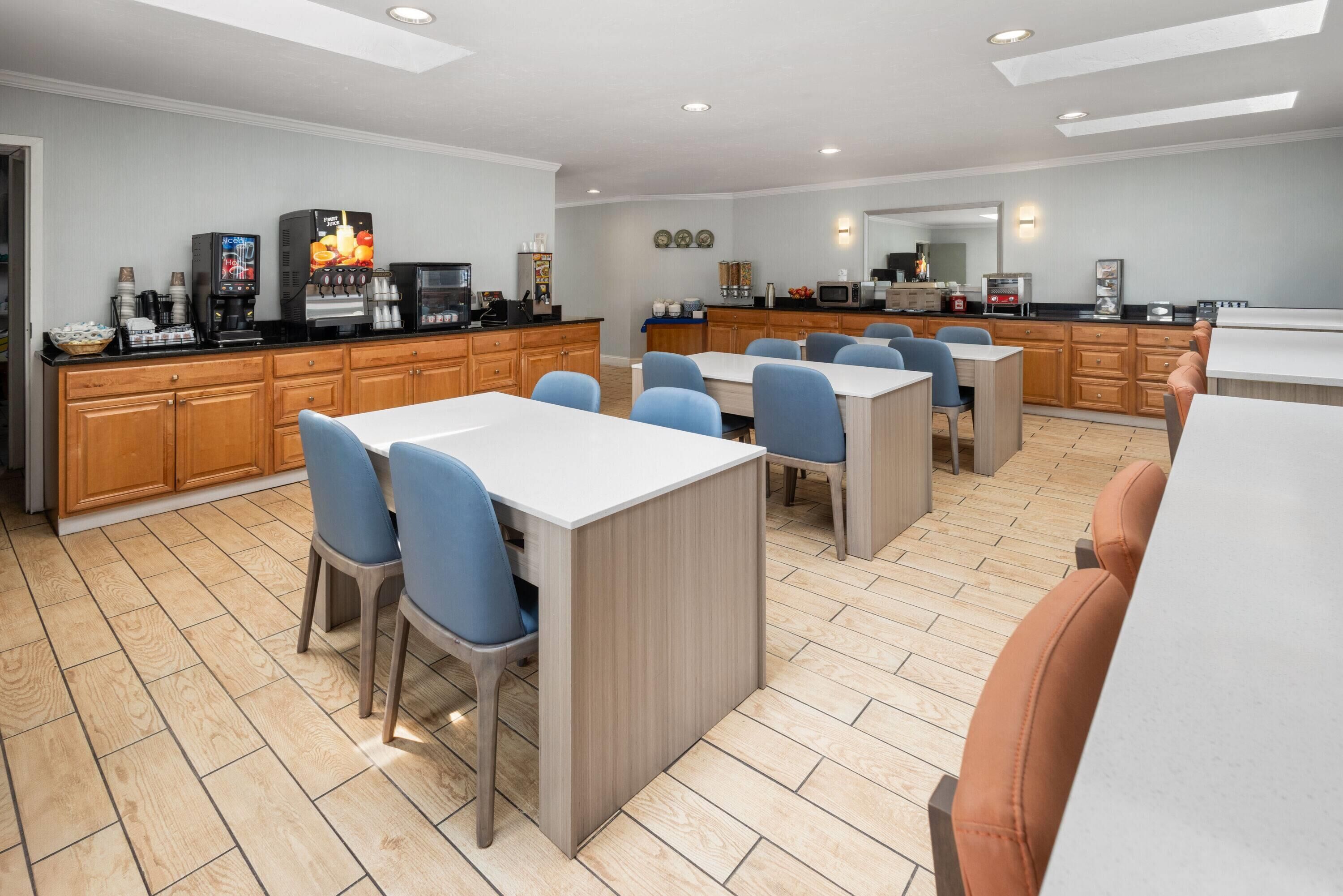 A modern kitchen with wooden cabinets, a coffee station, and a dining area with blue chairs and a white table.