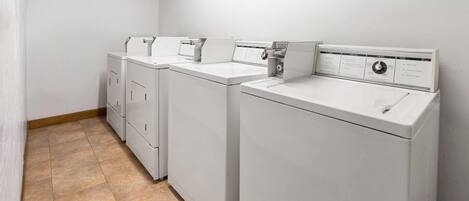 A laundry room with four white front-loading washing machines and a dryer.