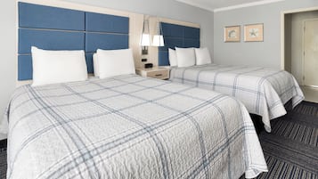 A hotel room with two beds, a nightstand, a lamp, and framed pictures on the wall.