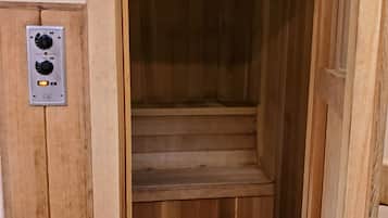 A wooden sauna with a control panel on the wall and a set of wooden steps leading into the sauna.