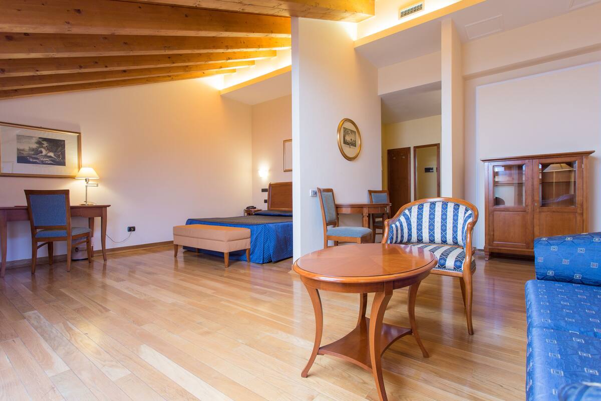 A spacious living room with a wooden floor, a round wooden table, and a blue patterned sofa.