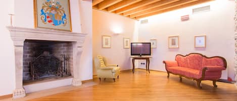 Una habitación amplia con chimenea, televisor, sofá rojo y cuadros enmarcados en la pared.