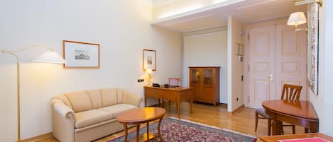Una sala de estar con sofá, mesa de centro, mesa de comedor con sillas, lámpara de pie y alfombra.