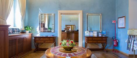 A room with a wooden round table, two side tables, a mirror, a fire extinguisher, and a bulletin board.