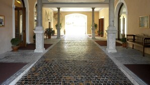 A corridor with columns, potted plants, and a tiled floor leading to an open area. - Grand Hotel Entourage Palazzo Strassoldo (Gorizia)