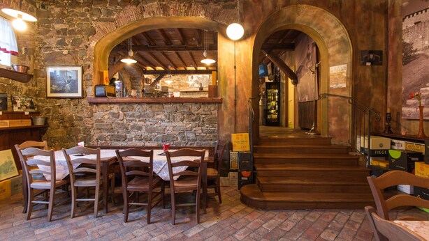 A rustic interior with stone walls, wooden tables, and a staircase leading to a bar area. - Grand Hotel Entourage Palazzo Strassoldo (Gorizia)
