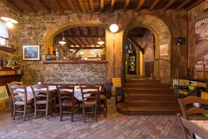 A rustic interior with stone walls, wooden tables, and a staircase leading to a bar area. - Grand Hotel Entourage Palazzo Strassoldo (Gorizia)
