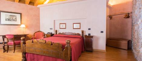 A bedroom with a wooden ceiling, a bed with a red bedspread, a desk with a chair, and a nightstand.