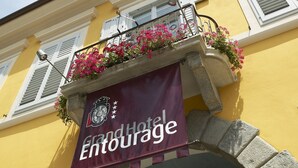 A hotel entrance with a yellow facade, a balcony with flowers, and a banner reading "Grand Hotel Entourage". - Grand Hotel Entourage Palazzo Strassoldo (Gorizia)