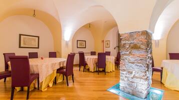 A dining area with multiple tables and chairs, a stone column, and framed artwork on the walls.