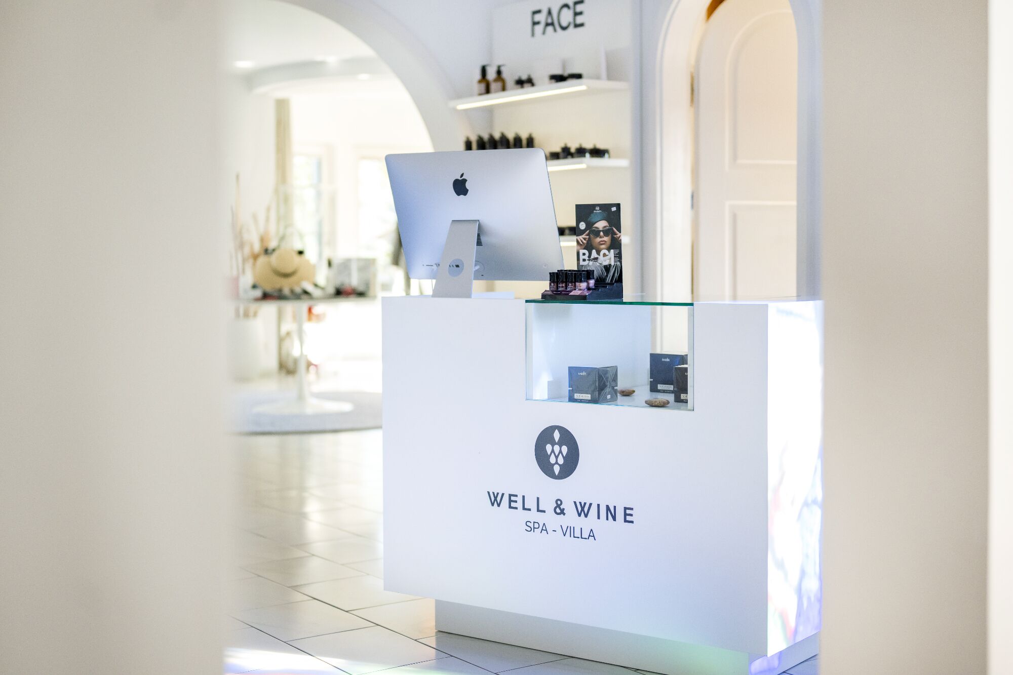 Un mostrador de recepción con el logotipo de 'WELL & WINE SPA - VILLA' y un monitor de computadora.