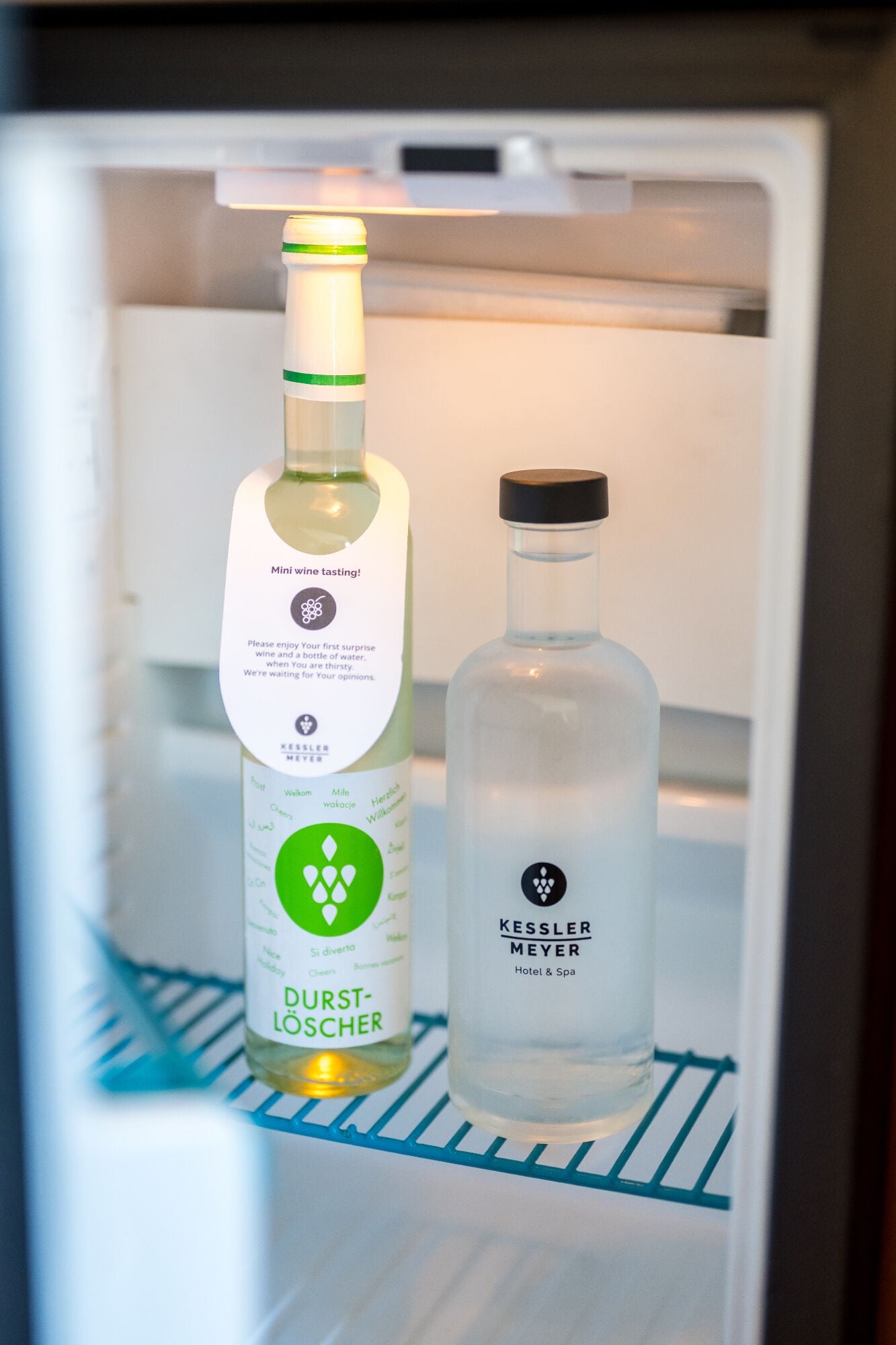 A mini wine tasting setup in a refrigerator with two bottles, one labeled 'Kessler Meyer Hotel & Spa' and the other 'Durst-Löschner.'