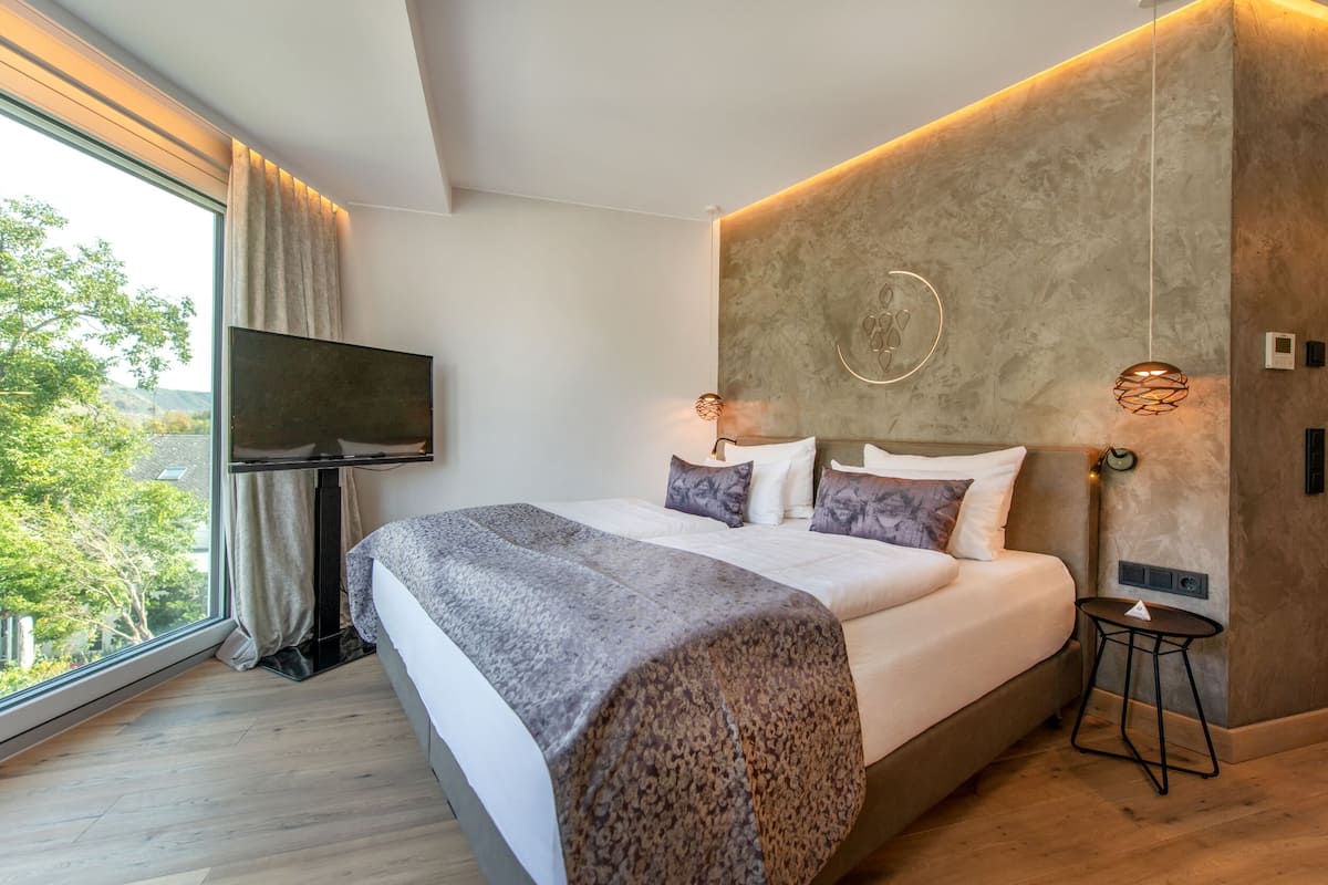 Ein modernes Schlafzimmer mit einem großen Bett, einem Fernseher und Blick auf Grünflächen.