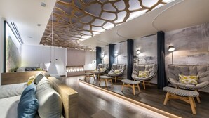 A modern living room with a wooden floor, a sofa with cushions, and four armchairs with cushions.